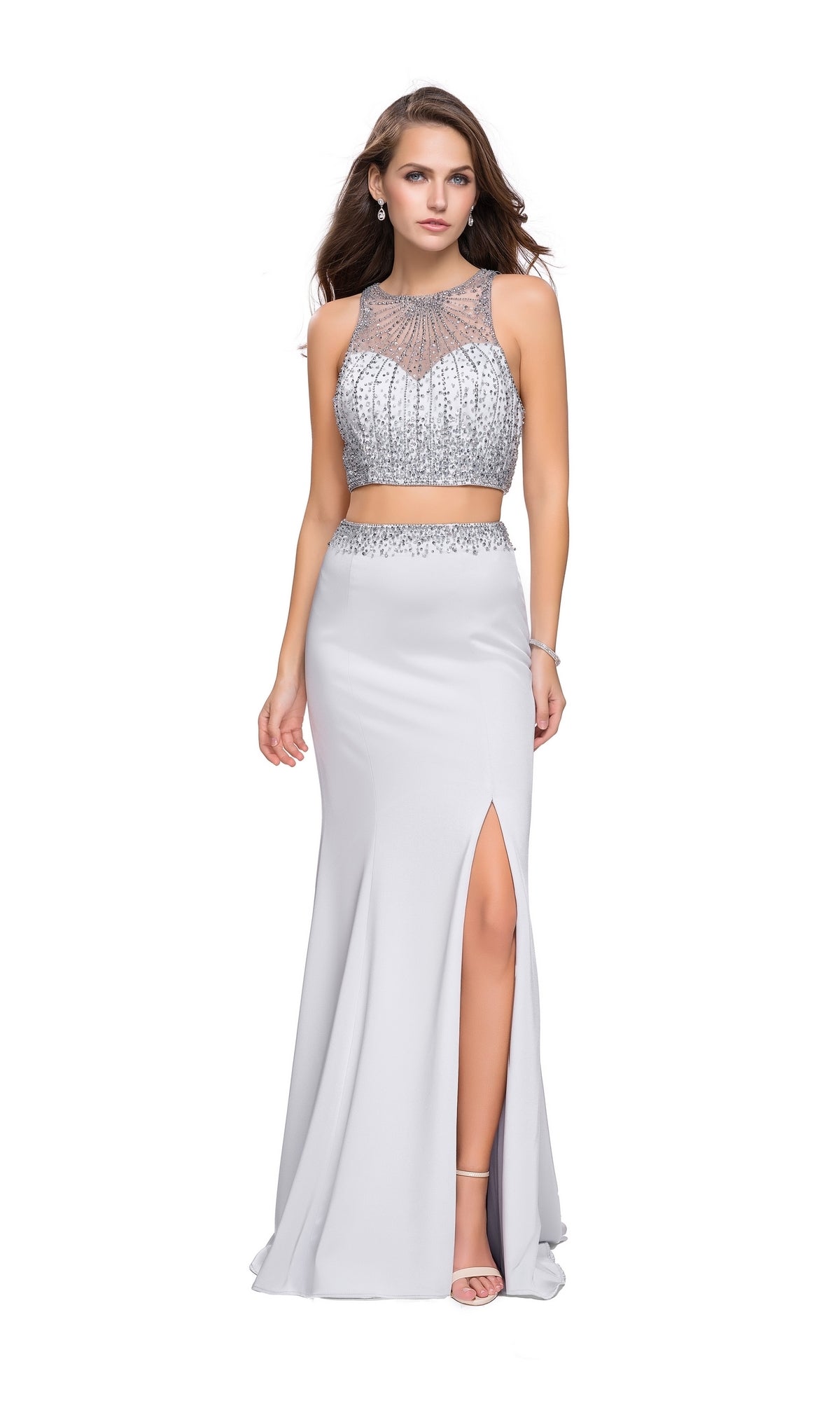 A woman models the La Femme Sheer High-Neck Two-Piece Prom Dress 26063, featuring a beaded crop top and matching high-slit skirt, standing against a white background.